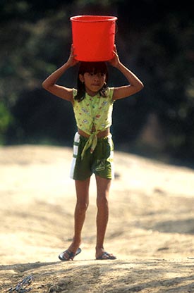 Girl carries bucket of water on her head.