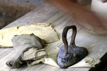 The hot iron rests on a cloth as the planchador rubs more sulfur powder into the brim.